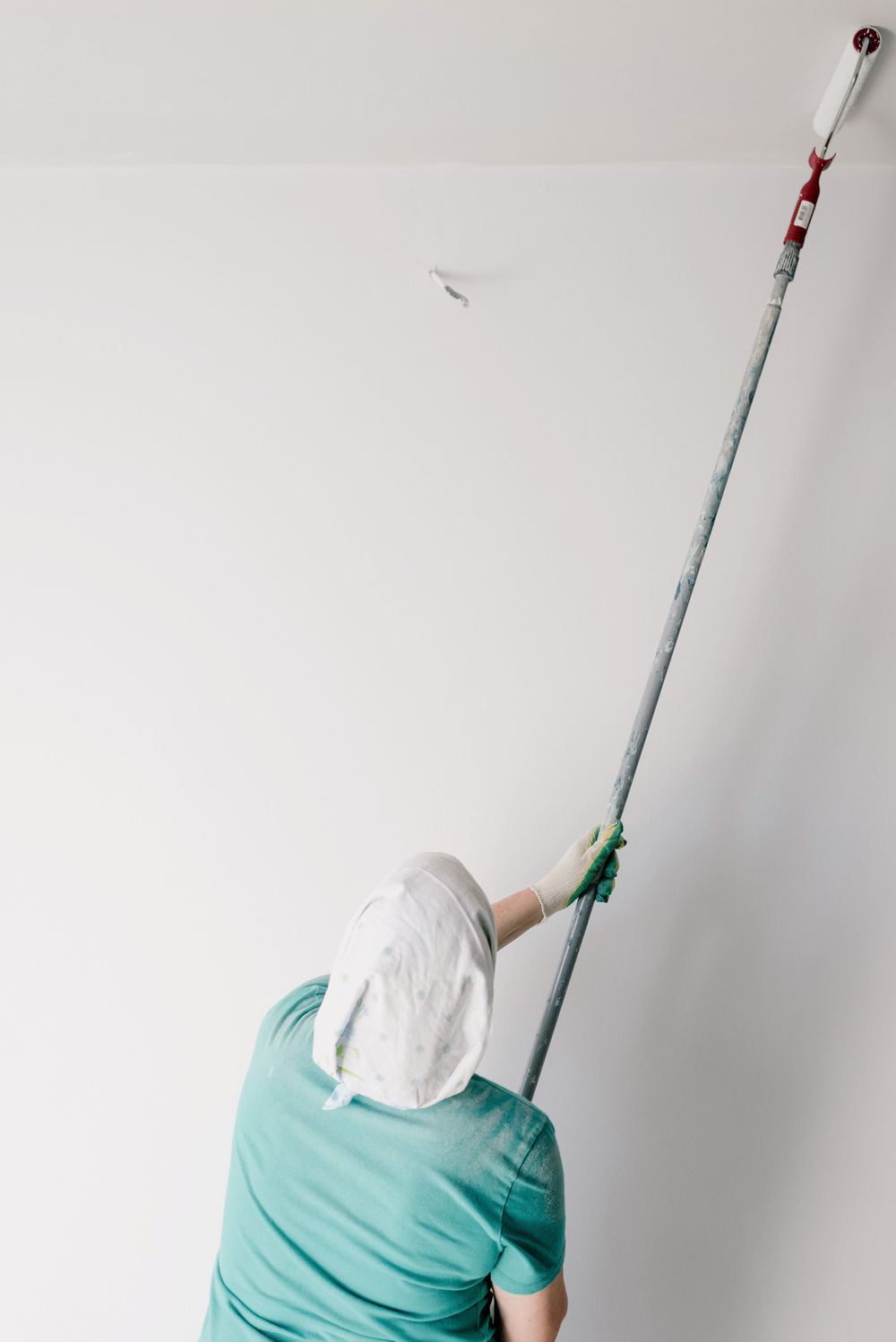 Een schilder rolt een plafond met een roller op een lange steel