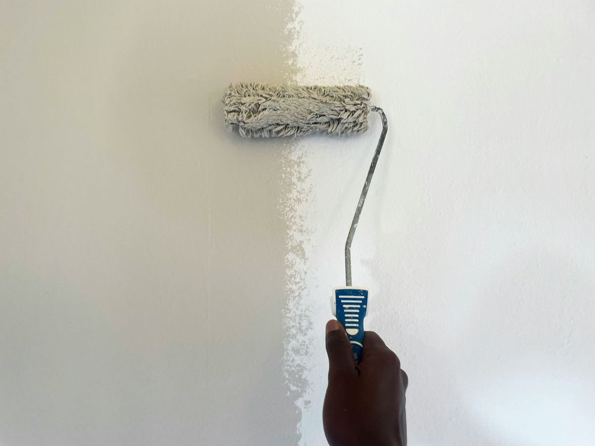 Een roller met witte muurverf over een muur, de helft is al geschilderd