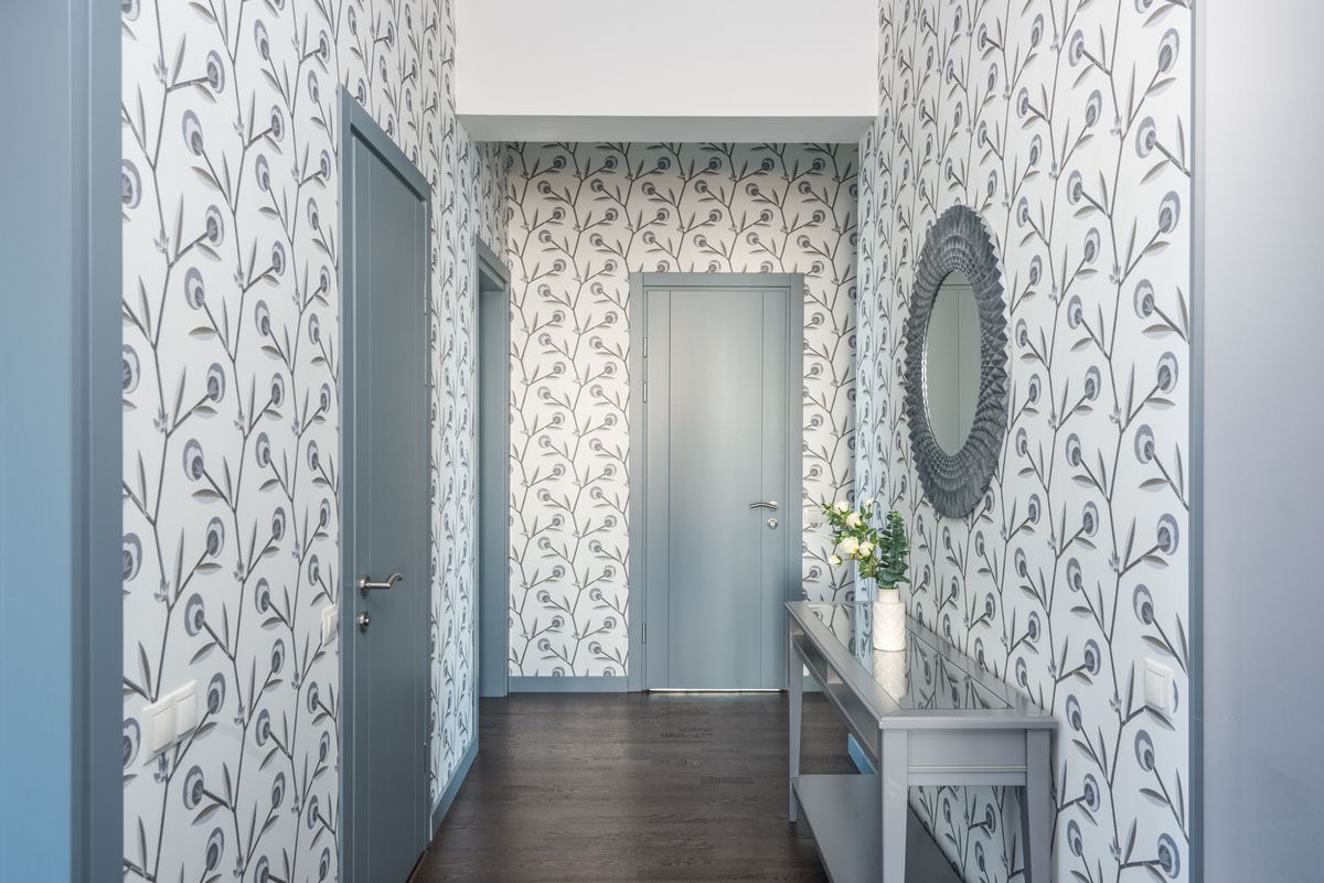 Een gang met grijs-wit bloemenbehang op alle muren en grijze deuren